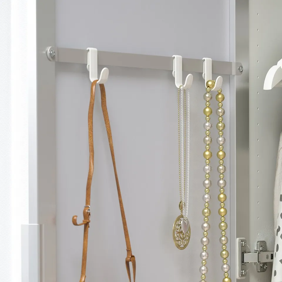 White hooks hold necklaces on a mirror cabinet, organising accessories in a space-efficient way.