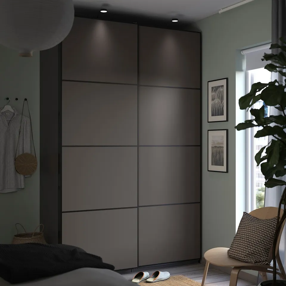 Modern minimalist bedroom with black PAX wardrobe, striped shirt, slippers, and potted plant by window.