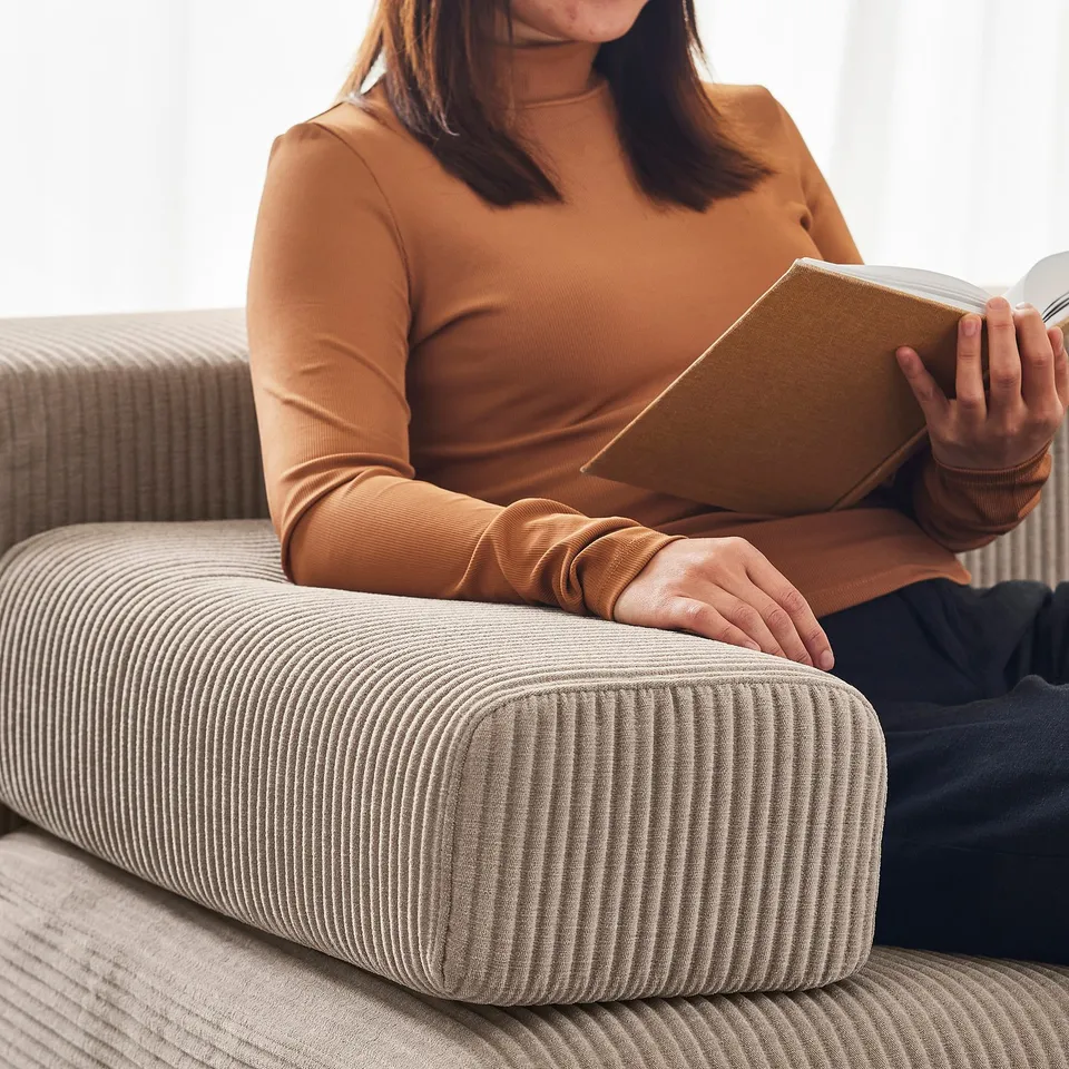 A person reads on a beige JÄTTEBO sofa, cuddling its cushion, relaxed in a cosy setting.