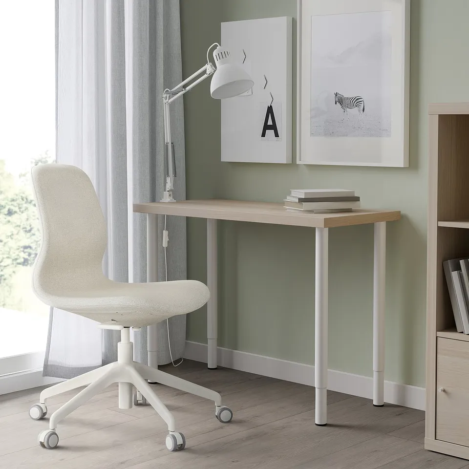 Minimalist home office with light wood desk, adjustable chair, lamp, books & artworks.