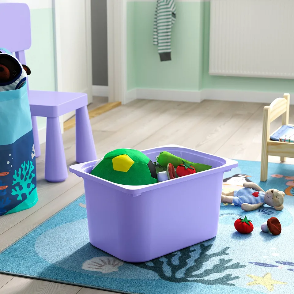 Purple TROFAST toy bin holds colourful toys on blue rug by chair.