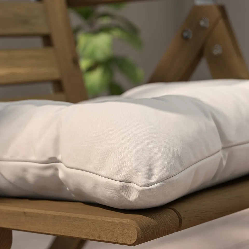 Close-up of a KUDDARNA outdoor cushion on a wooden chair. Soft, thick, white recycled fabric with secure ties, designed for durability in the sun.
