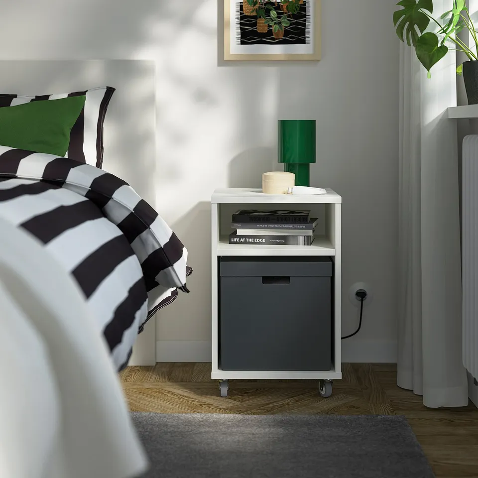 Bedroom with FJÄDERHARV box, books, green lamp, striped blanket, modern decor.