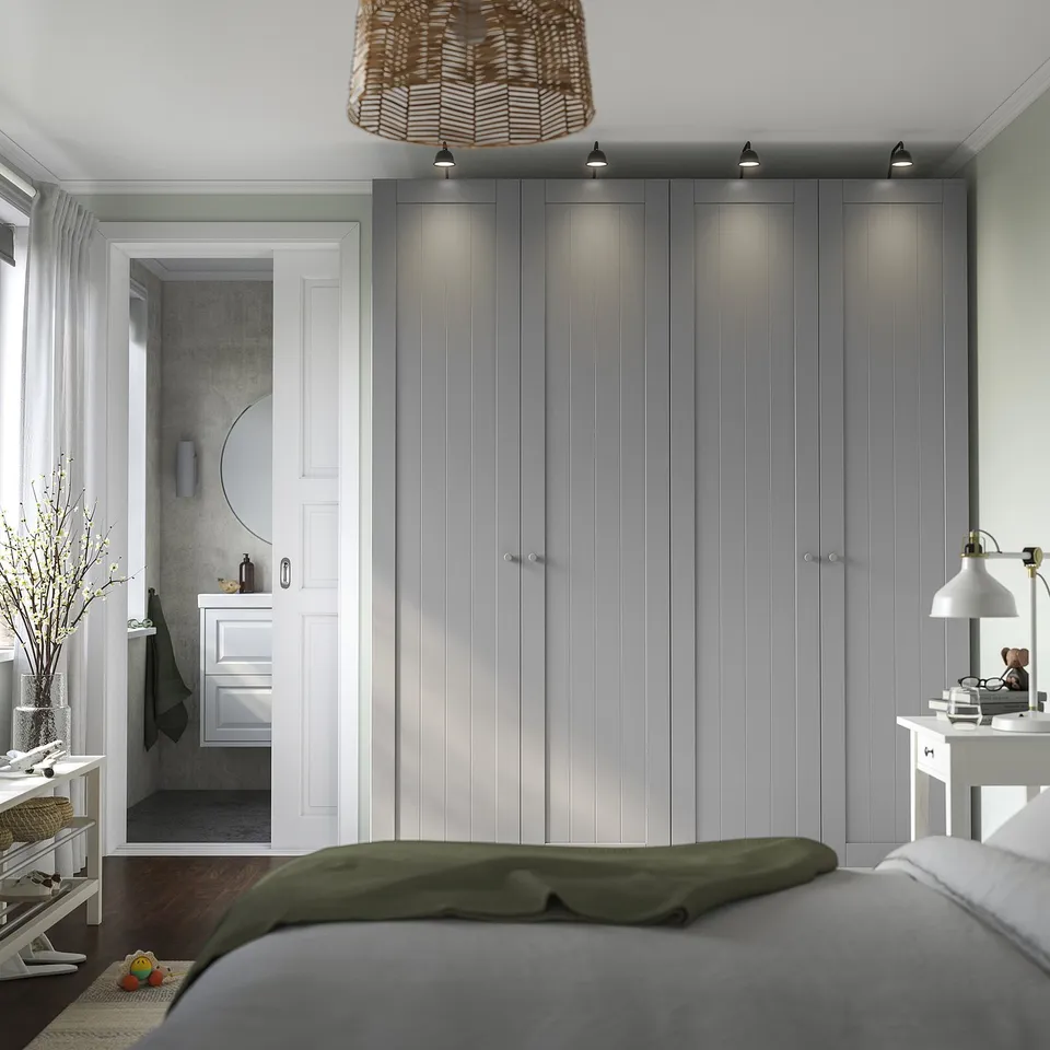 Modern bedroom with large grey PAX wardrobes, white nightstands, and a wooden bed. A white door leads to a minimalist bathroom.