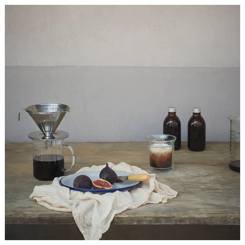 Silver coffee philtre, glass jar, fruits, and bottles on a wooden table.