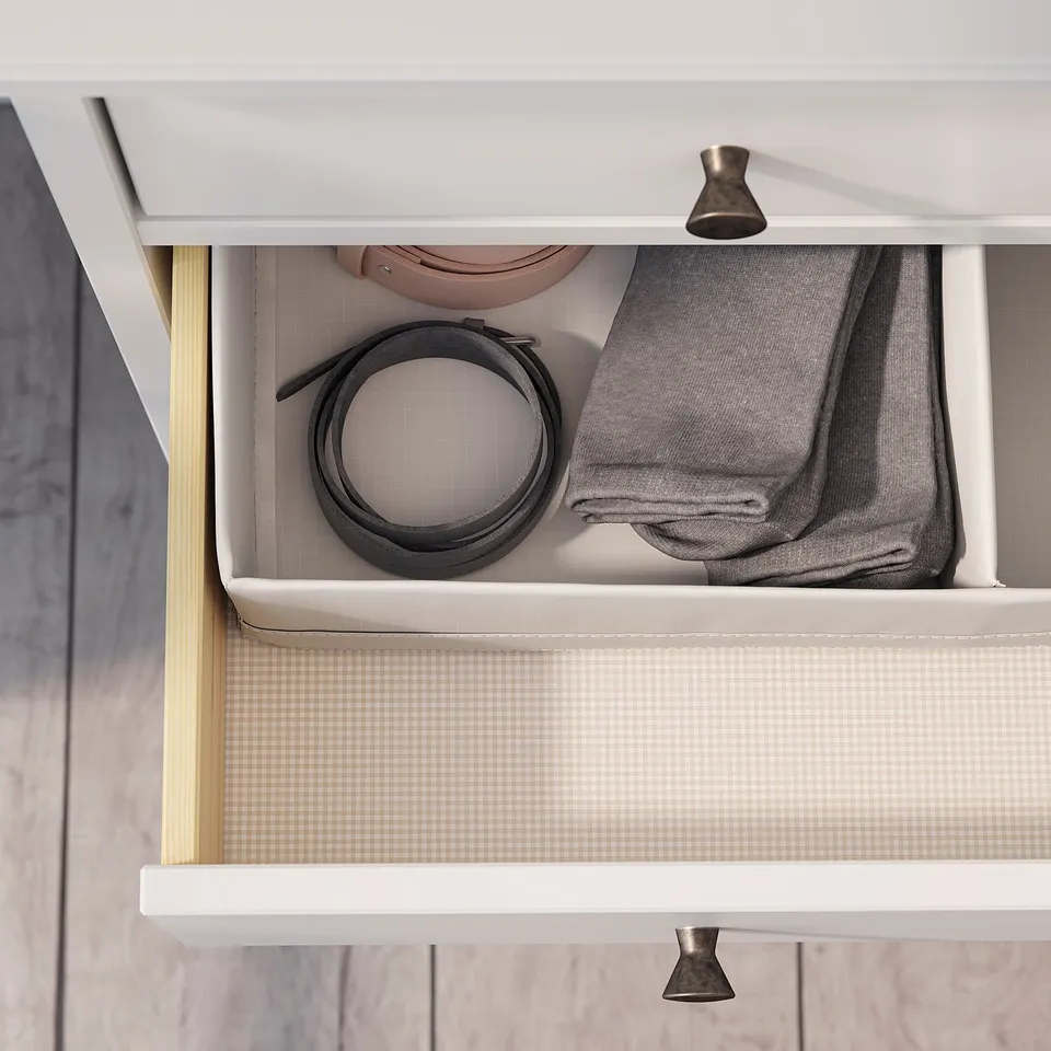 A white dresser drawer with grey contents: a rolled belt, folded scarf, and hat.