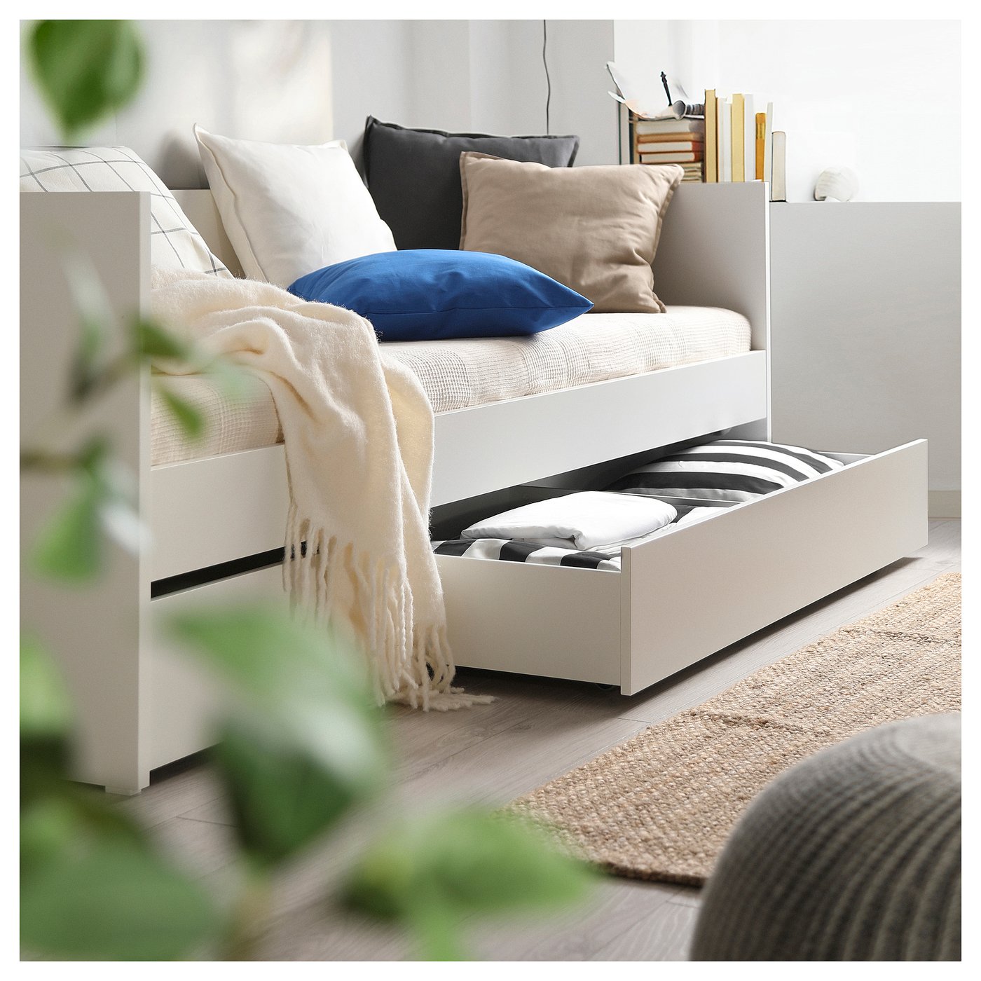 Modern white daybed with drawers, cushions, and blanket. Perfect for small spaces with organised storage.