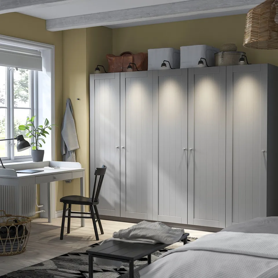 PAX wardrobes, grey, wooden, freestanding, shelves & rail. Topped with boxes, bags, lantern. Desk with chair, window, plant basket.