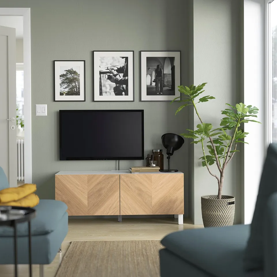 Modern living room with BESTÅ tv stand, blue couch, yellow pillow, black lamp, photos, and green plant in basket.