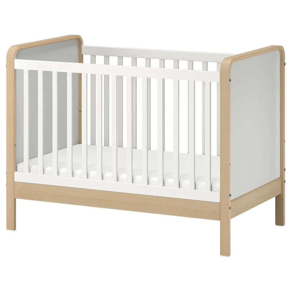 Wooden baby crib with white sides, minimalist design, rounded edges, vertical slats.