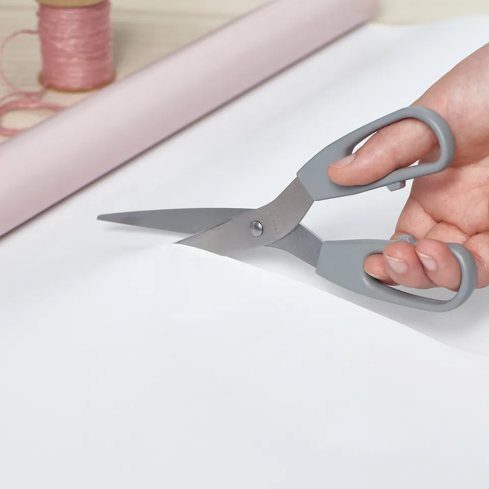 A hand holds gray-handled scissors, cutting paper, showcasing versatile utility.