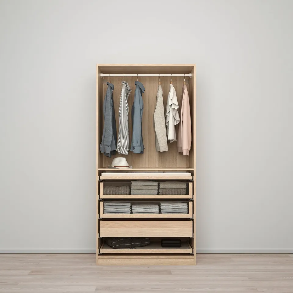 A modern wooden PAX wardrobe organises clothes neatly. It hanging garments, folded clothes in drawers, and shelf storage.
