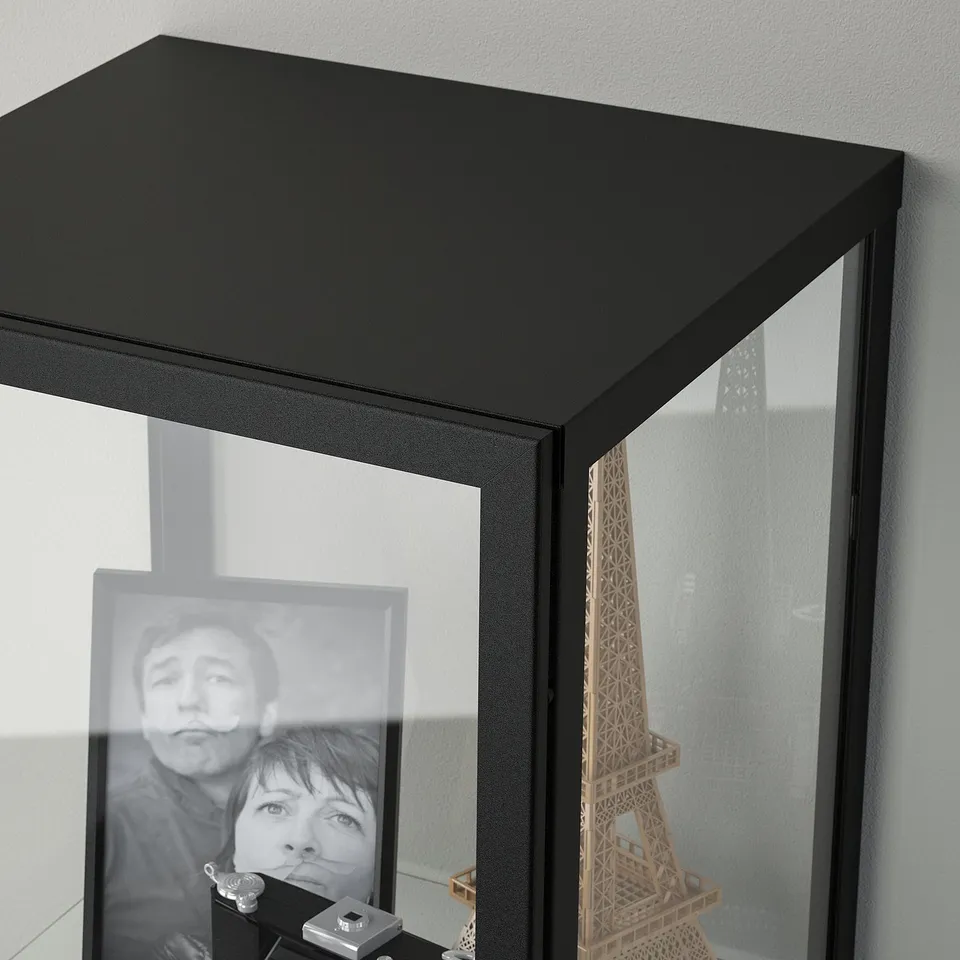 Black glass-door cabinet displays photo and eiffel tower model.