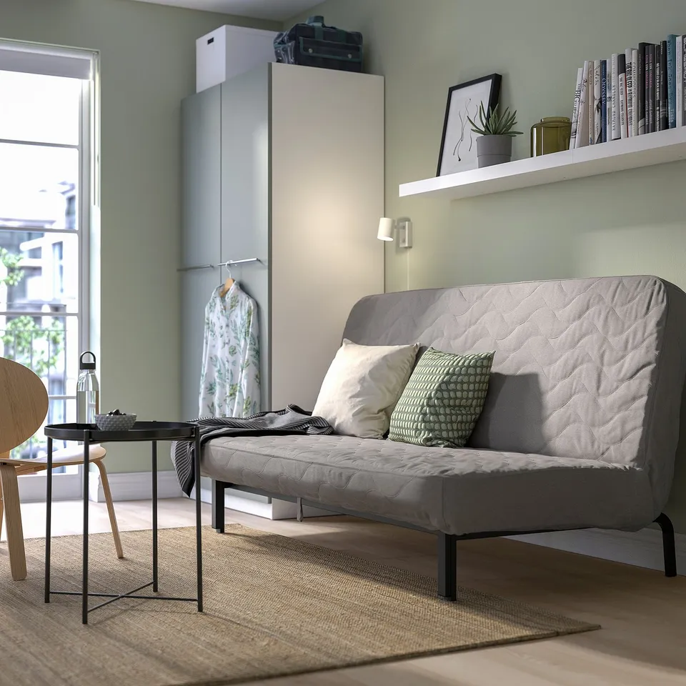 Modern living room with NYHAMN sofa-bed, cushions, coffee table, and bookshelf with plant.