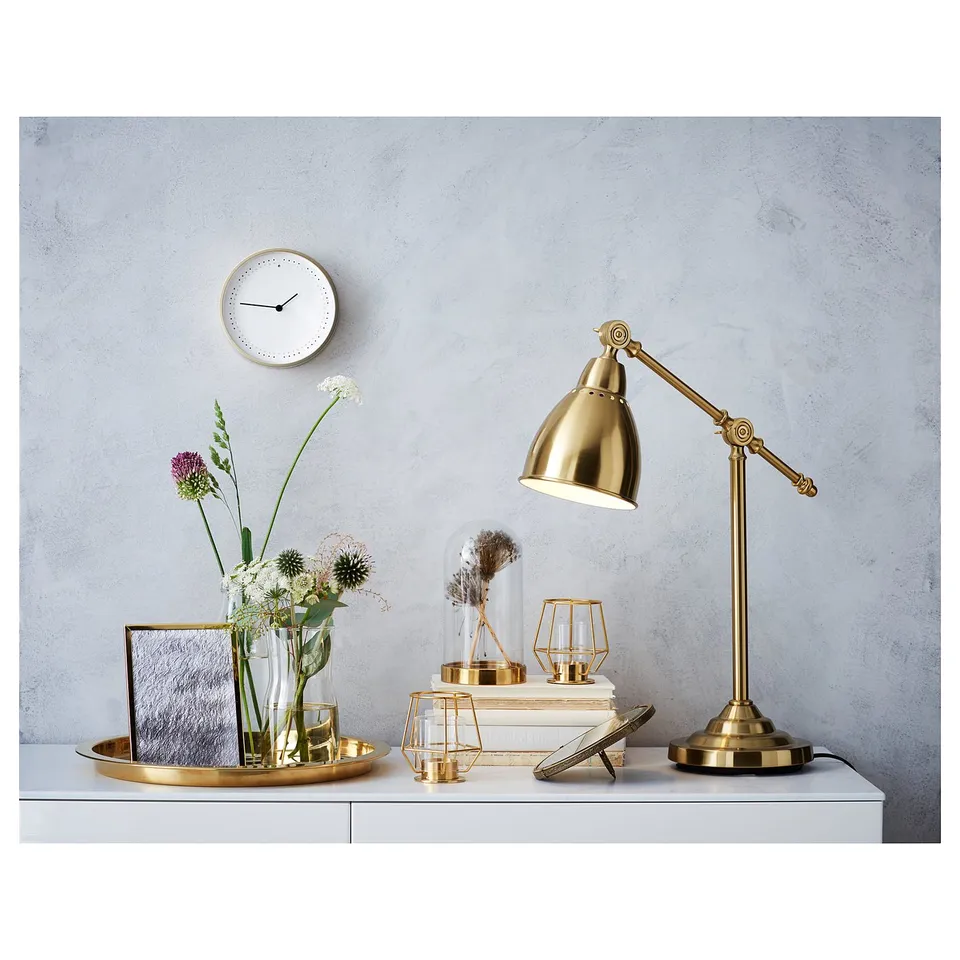 Gold desk lamp, white clock, glass vase with flowers, decorative items on table.