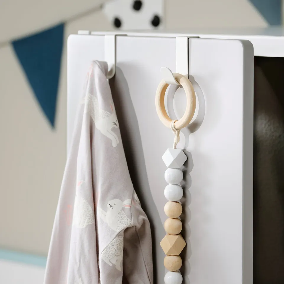 White LÄTTHET wall hook holds a pink and white blanket with a cat design and a wooden and grey bead teething toy.