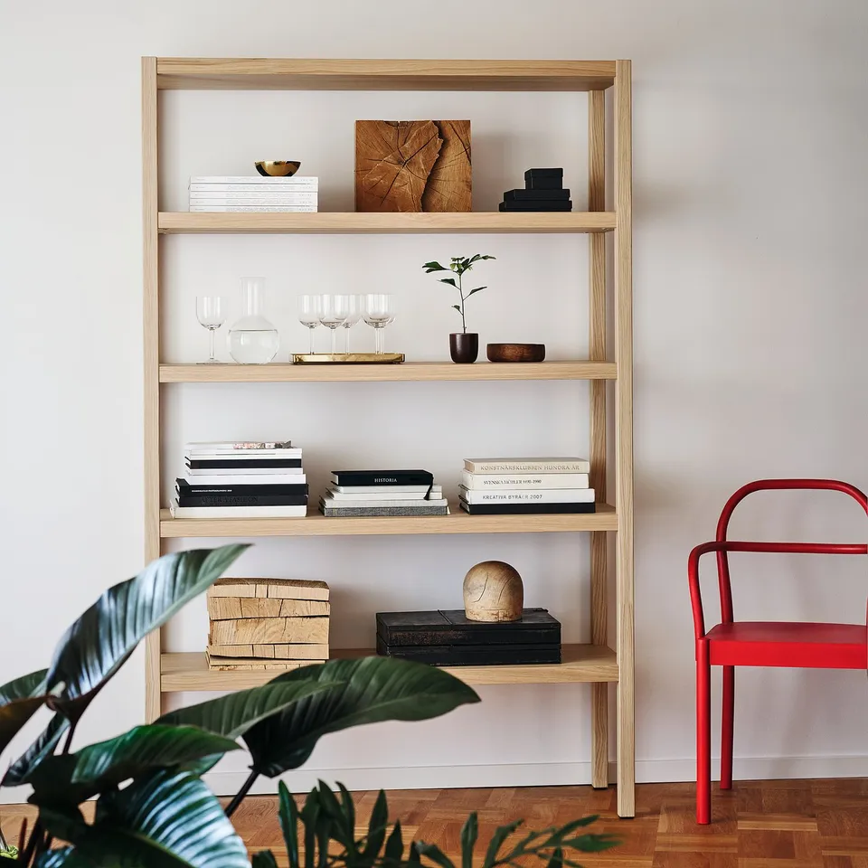 Oak shelves with books and decor, red chair, plant; minimalist