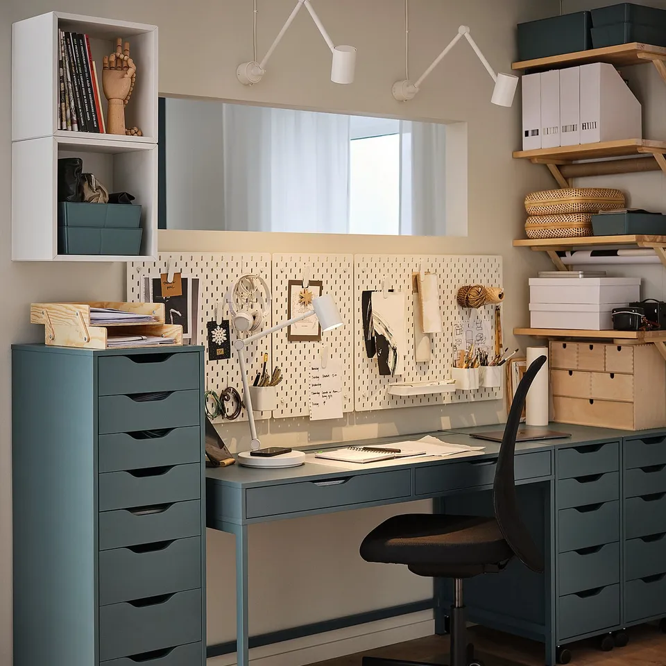 Modern home office featuring SKÅDIS blue-green pegboard setup, black chair, and grey desk with organised storage shelves and a whiteboard.