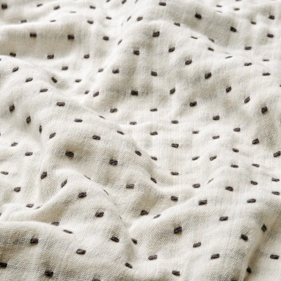 Off-white bedspread with delicate dark grey stitching, showcasing smooth, durable cotton texture.