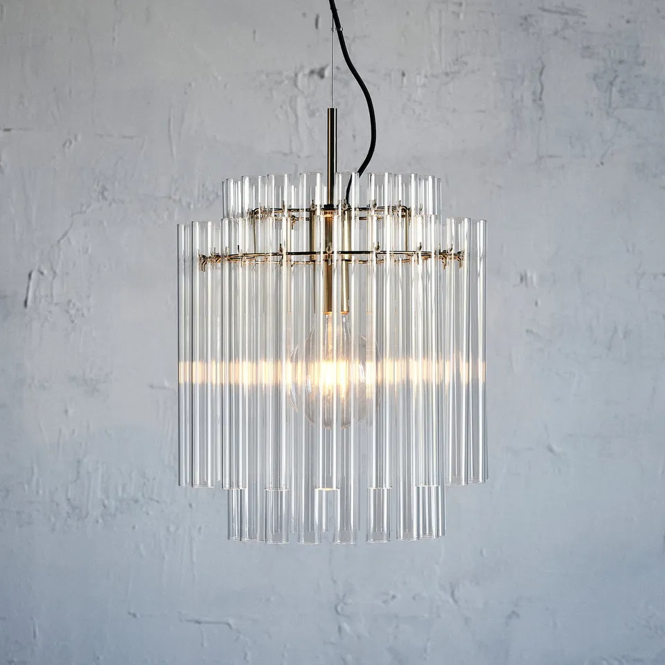 Modern chandelier with clear glass cylinders hangs on a metal hook, emitting warm light.