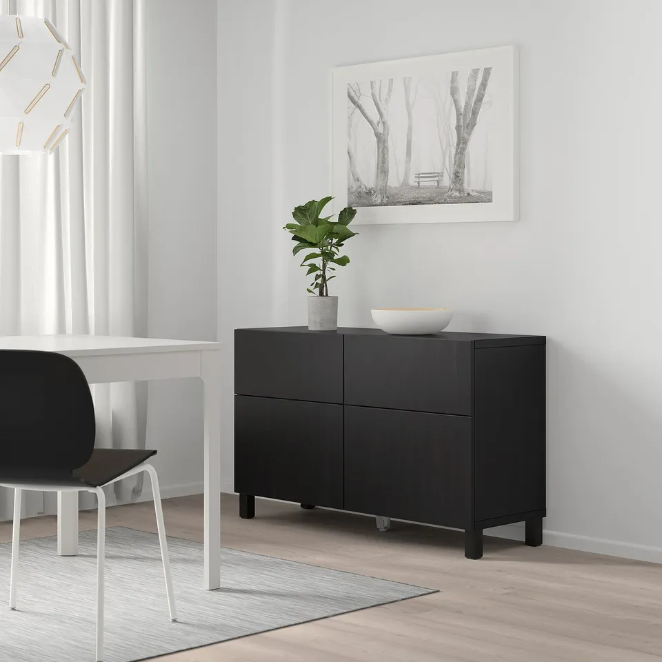 Black BESTÅ unit with plant, bowl, near table, chair, under tree print.