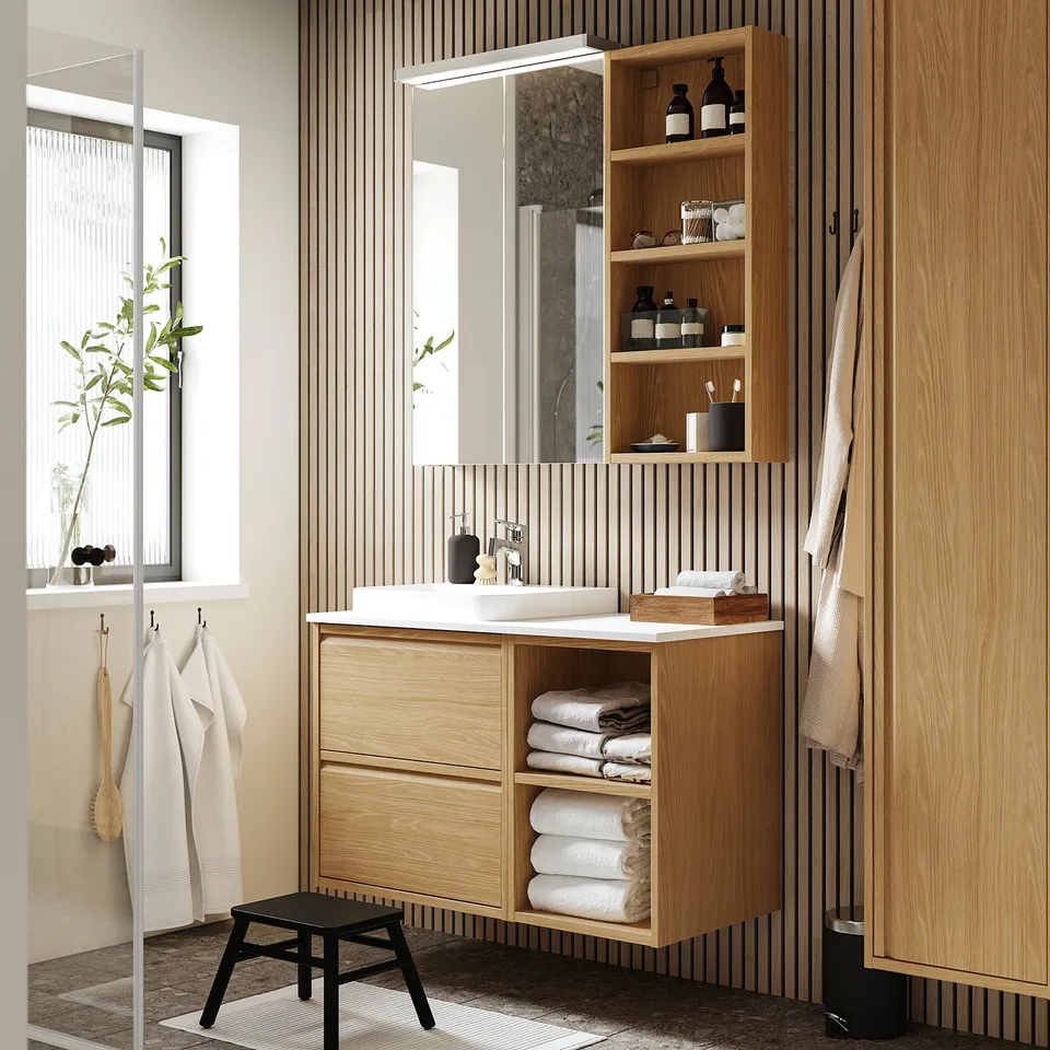 Light wood bathroom vanity with marble sink, storage, and mirror.