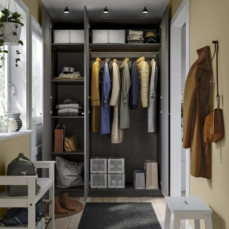Open wardrobe with hanging jackets, folded clothes, handbags, and storage boxes. Shelf with hats, and a stool nearby.