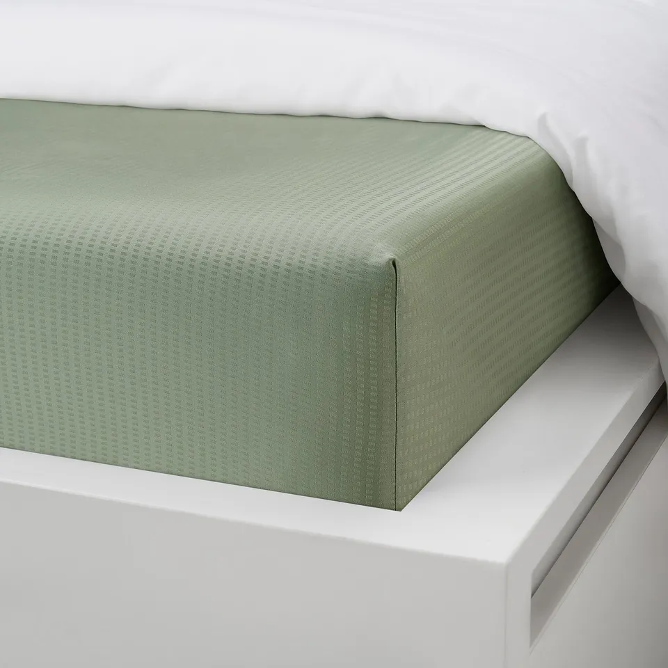 Green fitted bed sheet on white bed, showing elastic edges and smooth fabric.