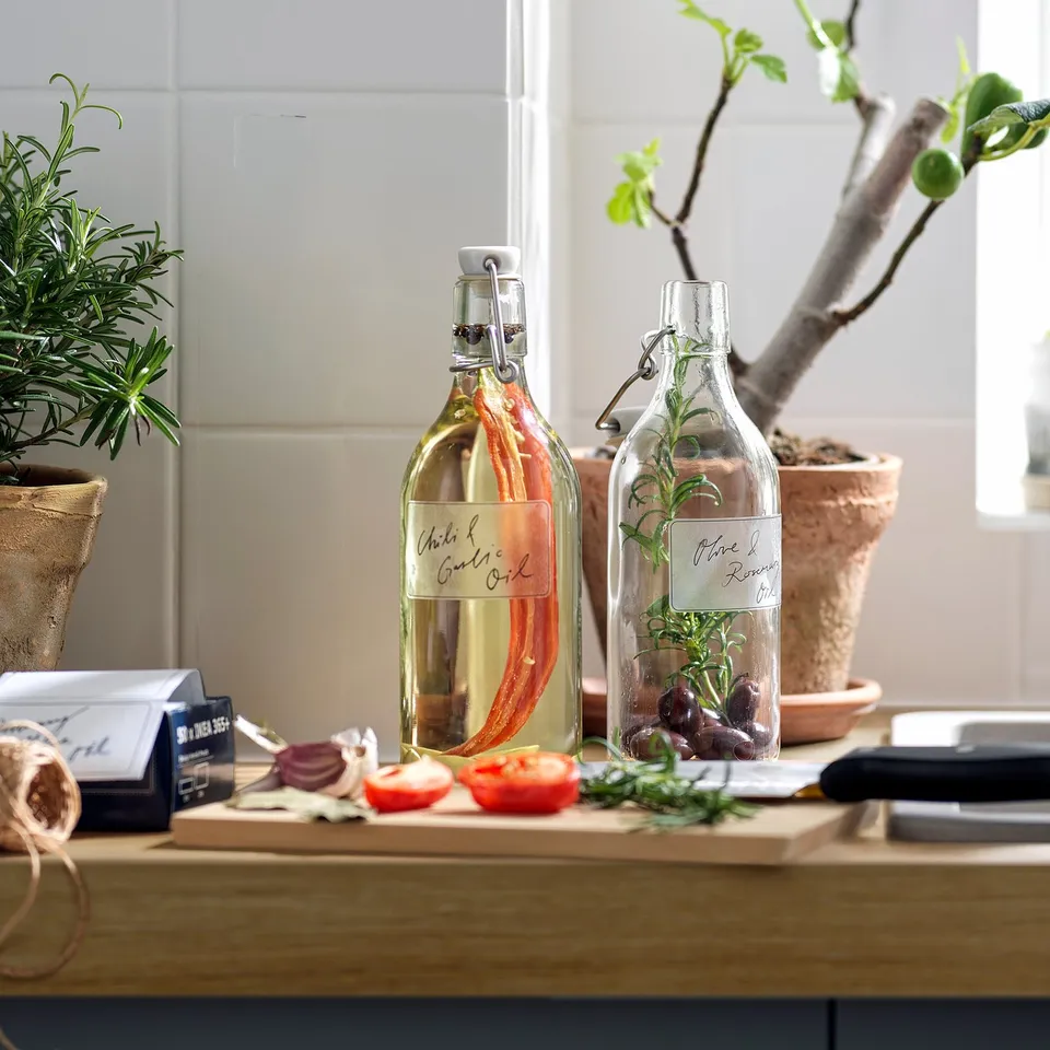 Two glass bottles with labels chile & garlic oil and olive & rosemary oil on a kitchen countertop, sealed with tight-fitting stoppers.