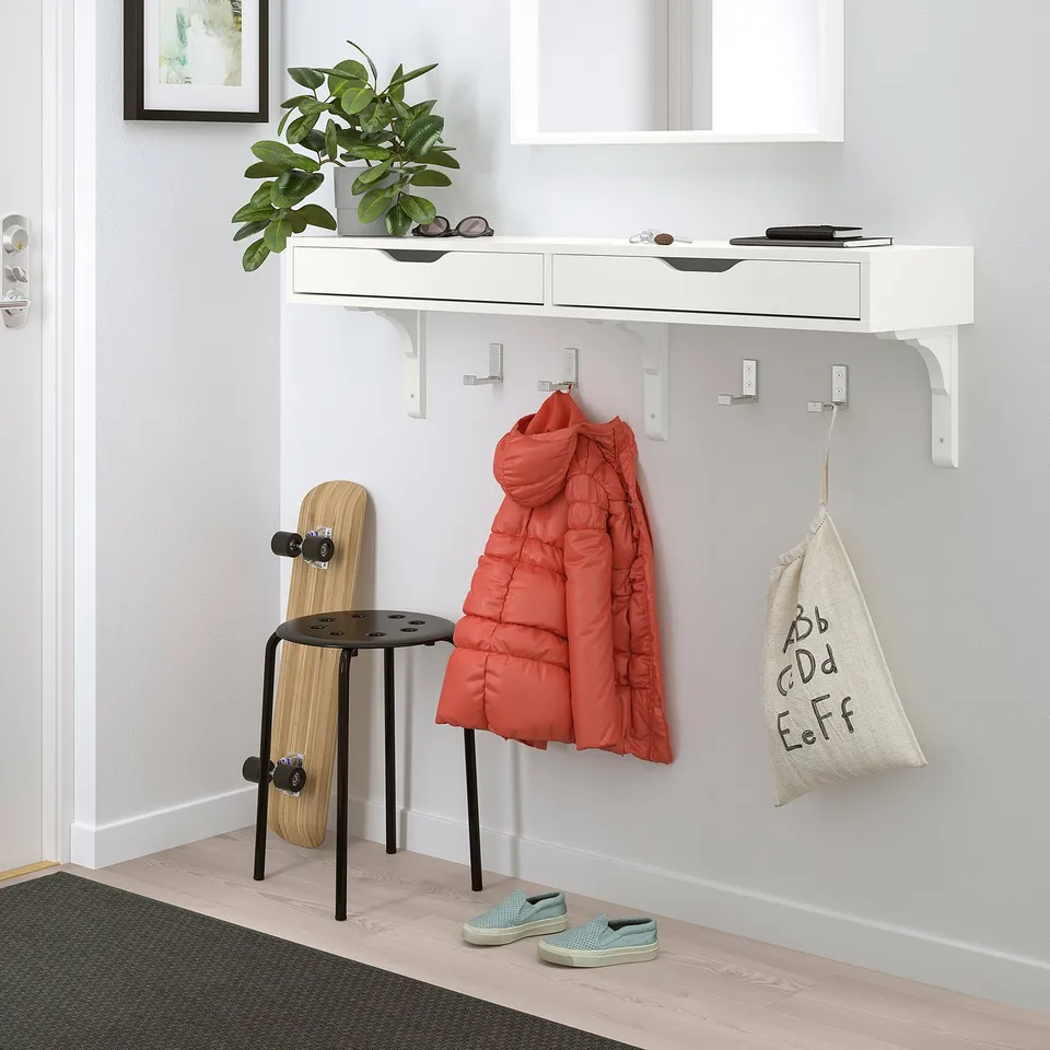 White EKBY ALEX shelf with red jacket, bags, and skateboard. Small stool beside.