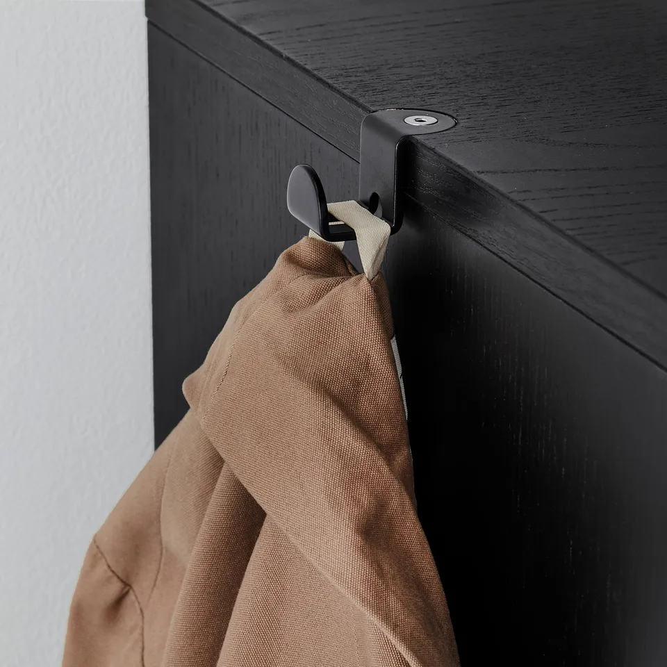 Brown fabric bag hangs on black metal hook attached to side of dark wooden cabinet.