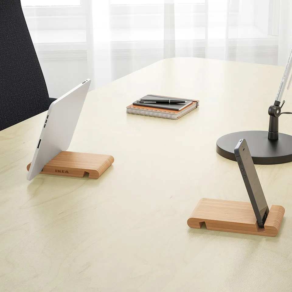 Light wooden desk with two BERGENES stands holding a laptop and tablet. A notepad and pens are also visible.