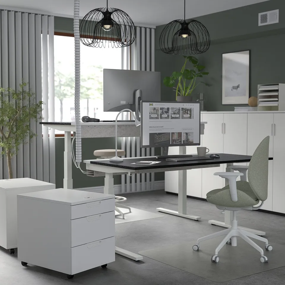 MITTZON white sit/stand desk with dual motors and green ergonomic chair. Modern office setup with large monitors.