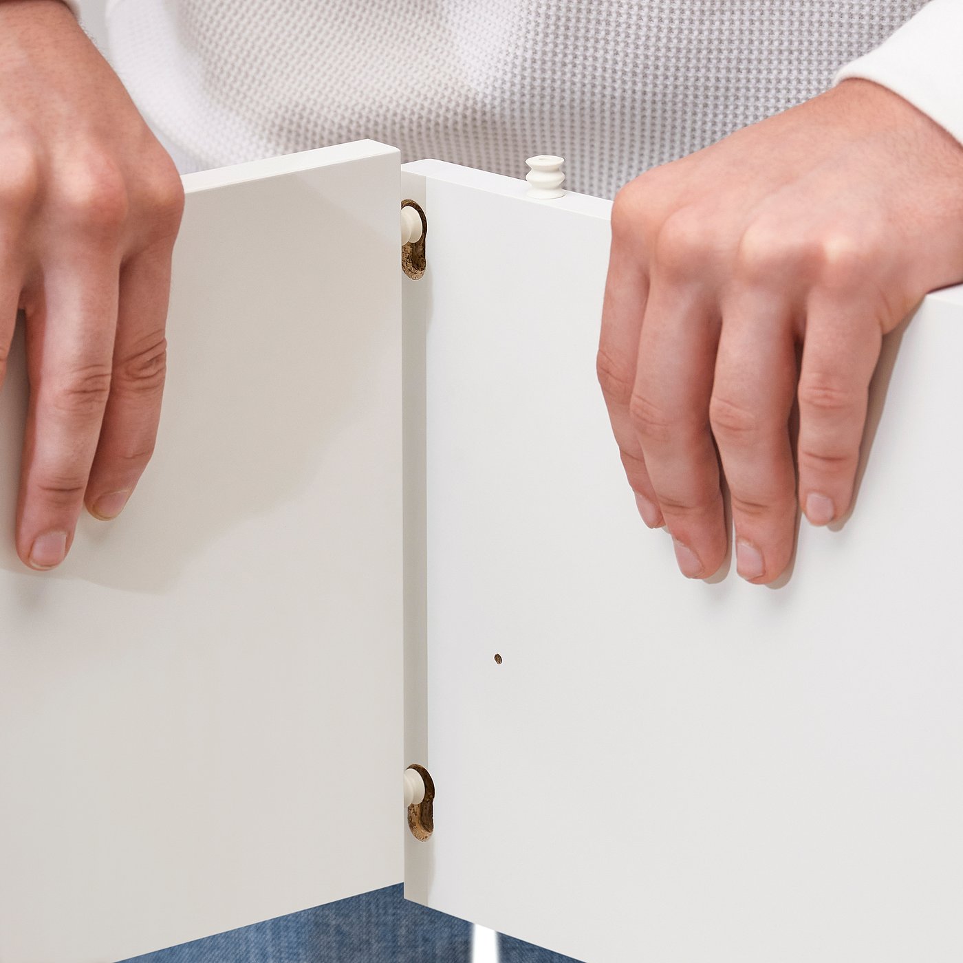 Assembling VIHALS white storage unit with wooden panels and metal hinges.
