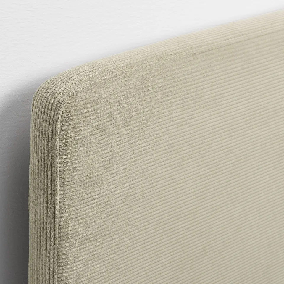 Close-up of a soft, light-colored bed frame with a ribbed, textured headboard. High-quality fabric, neatly stitched edges.