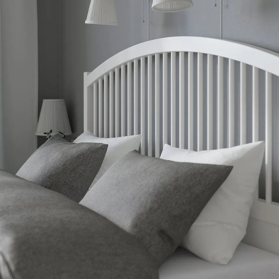 Bed with arched headboard, grey pillows, soft lighting, plush bedding.