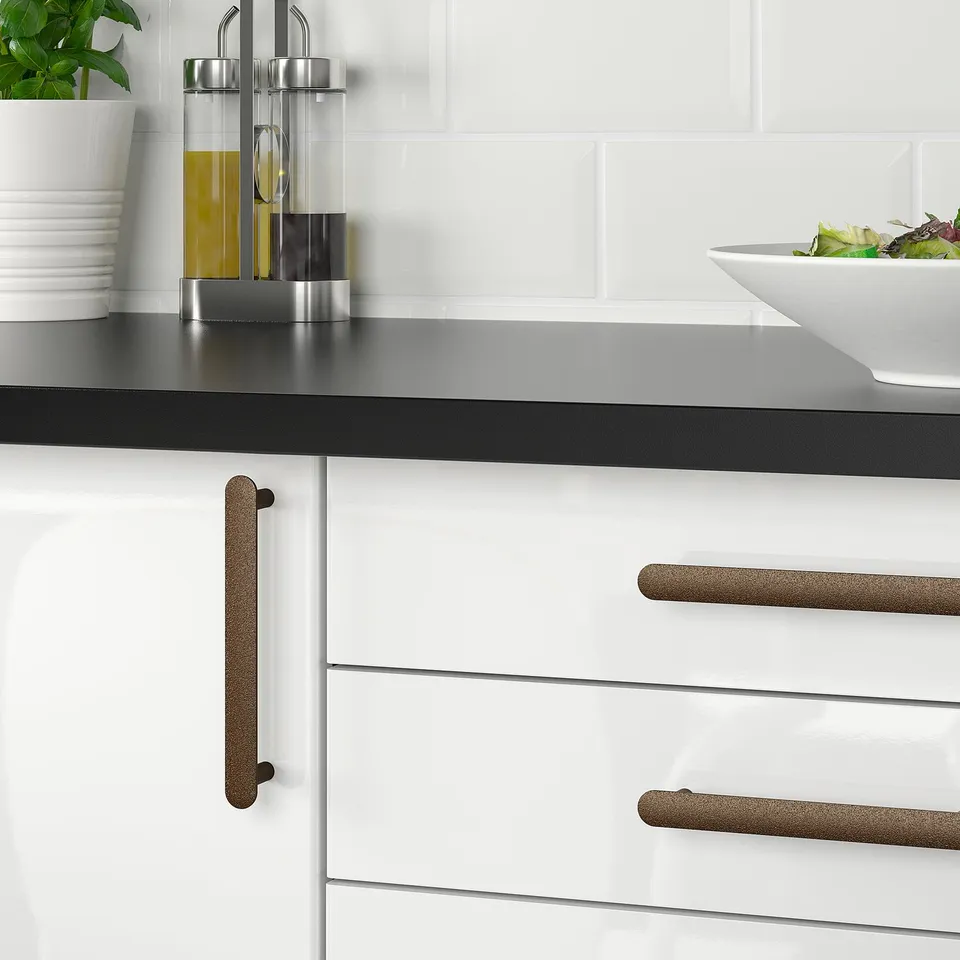 Modern kitchen with NYDALA handles. Dark counters, plant, oil, salad. Aluminium handles are sleek.