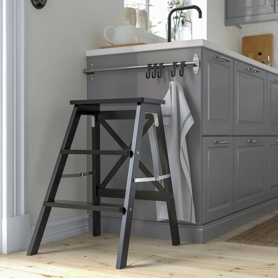 Black BEKVÄM step ladder near grey cabinets. Folded, modern, with high-storage striped towel.