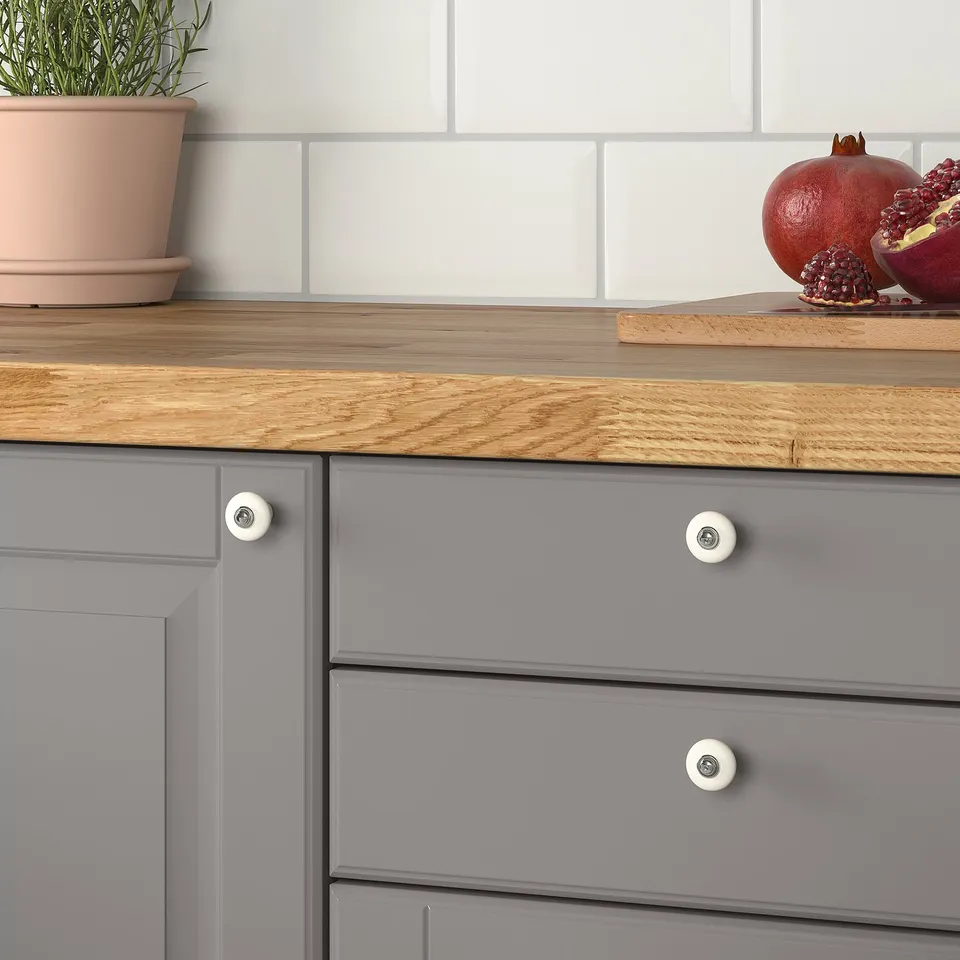 Grey cabinets with wood countertop, white knobs, potted plant, and pomegranate.