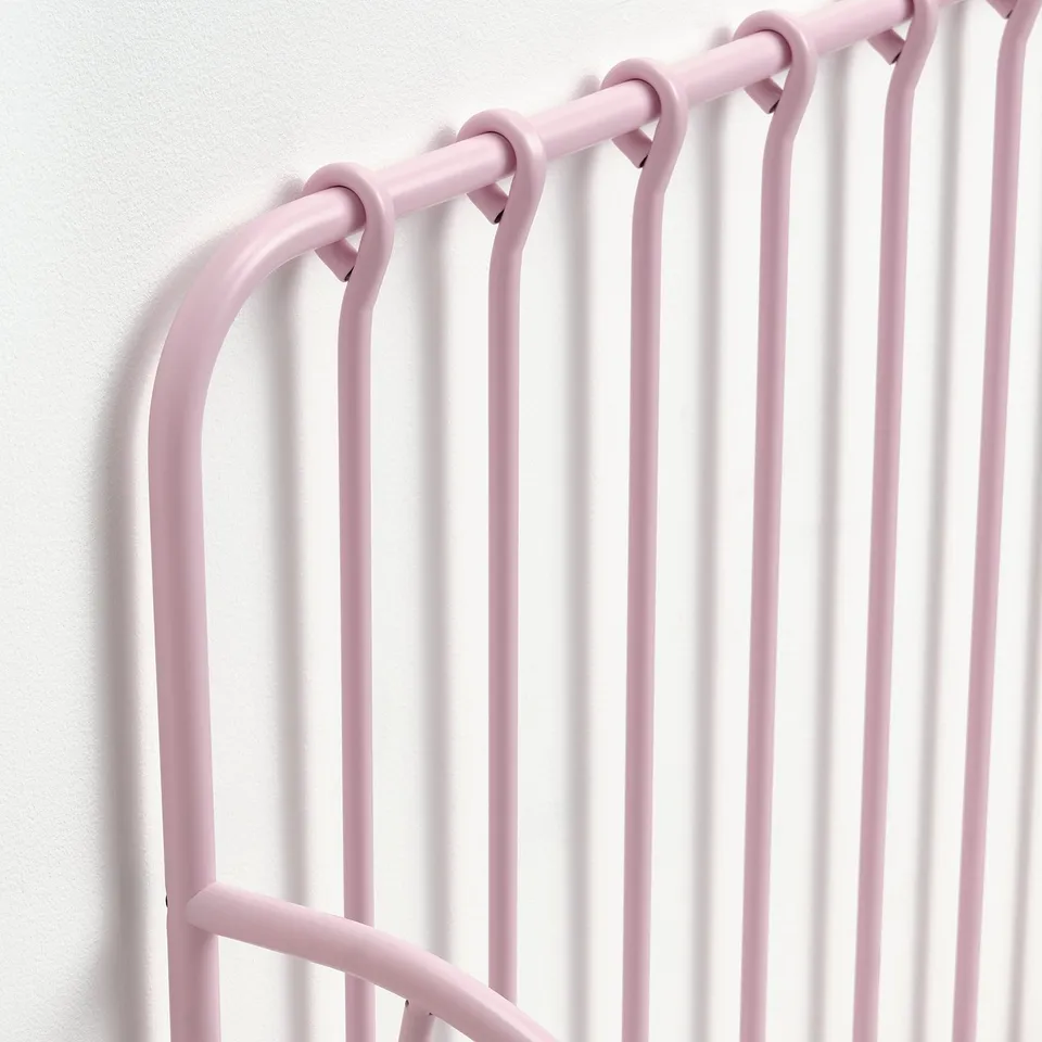 Light pink metal bed frame with rounded bars, mounted on a white wall, showcasing sturdy and modern design.