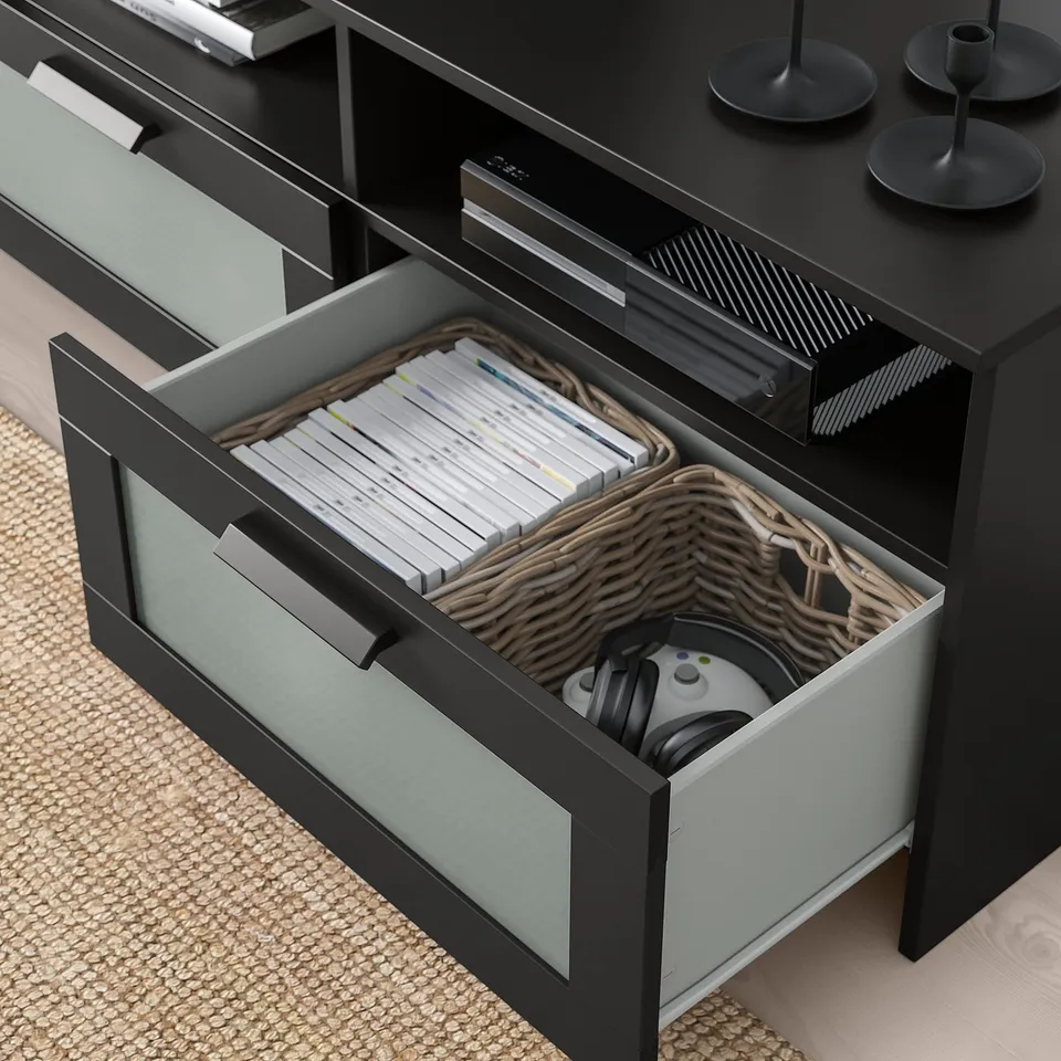 Open drawer of black tv unit reveals organised game controllers, headphones, and discs in a woven basket.