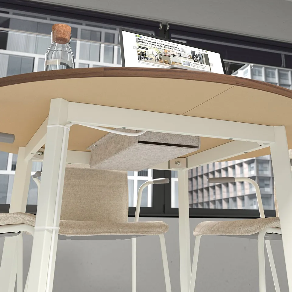 Modern round conference table with white legs, beige top, two stools, and cable compartment. City view.