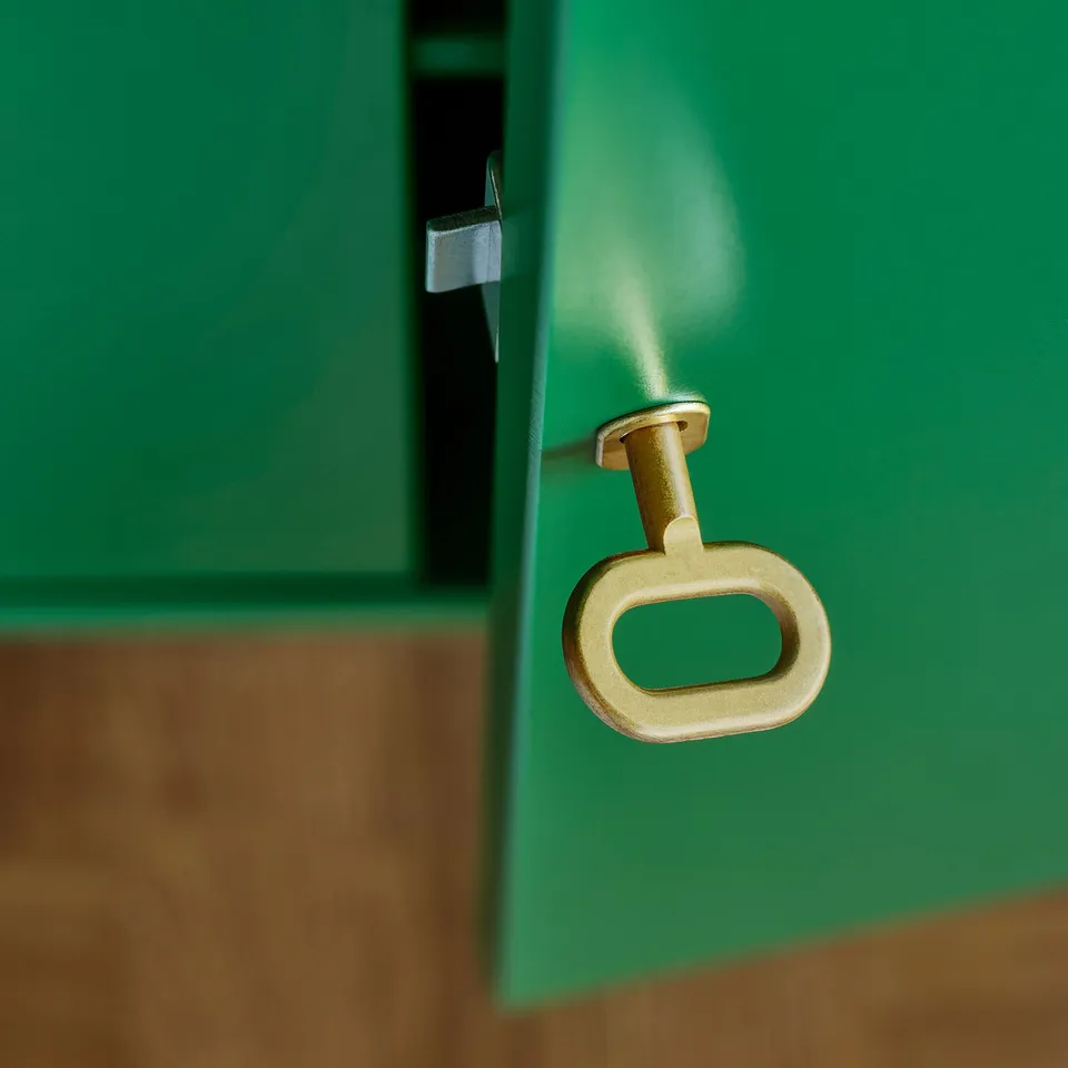 Golden metal handle on bright green cabinet drawer, reflecting quality and style.