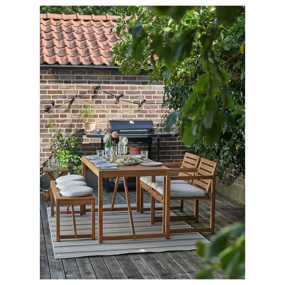 Outdoor patio set with wooden table and chairs, cushioned seats. Set near brick house and grill.