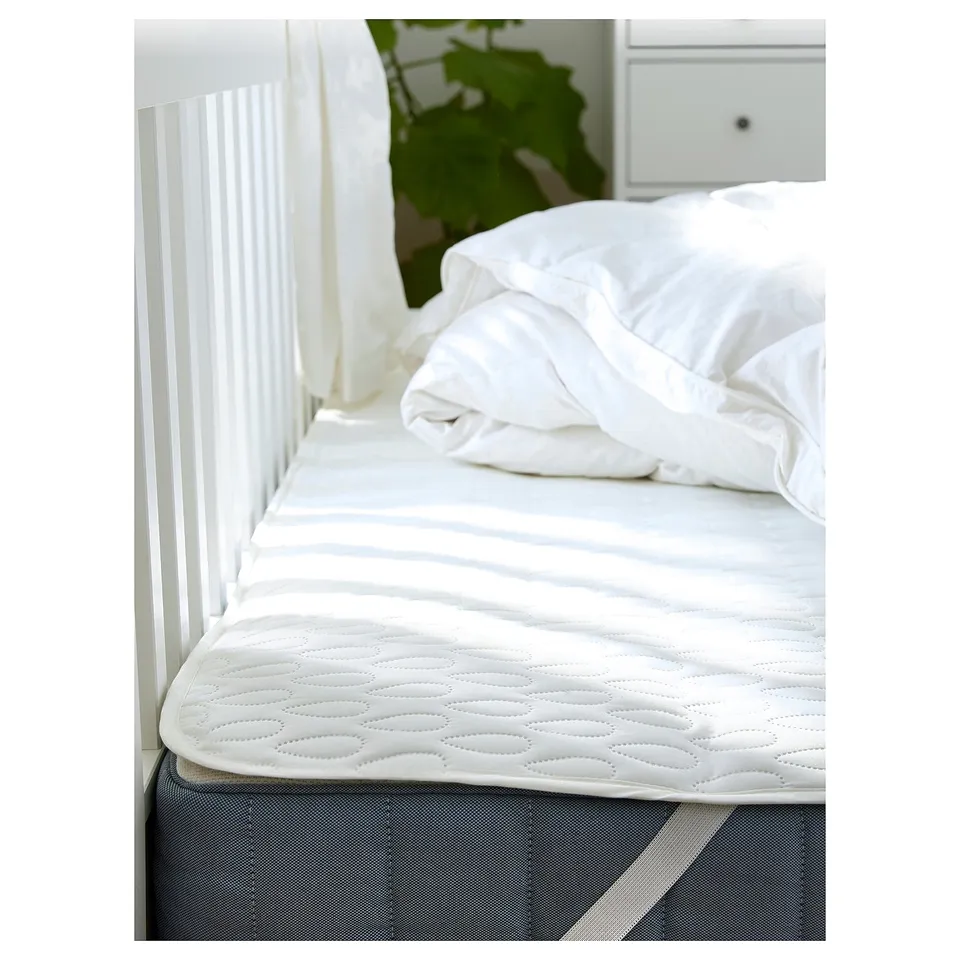 Clean bed with white protector, plant, white sheets, wooden headboard.