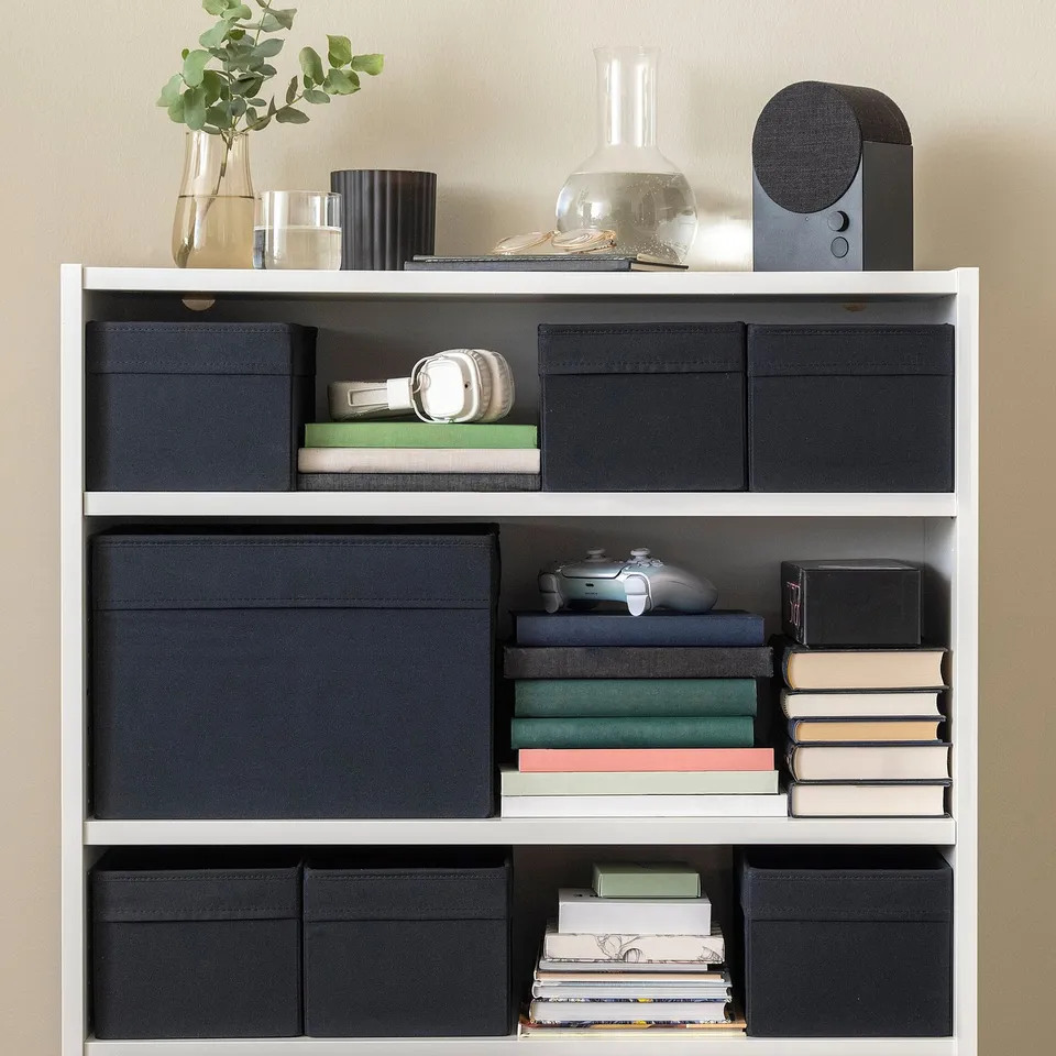 Bookshelf with black fabric storage boxes, books, headphones, and decorative items.