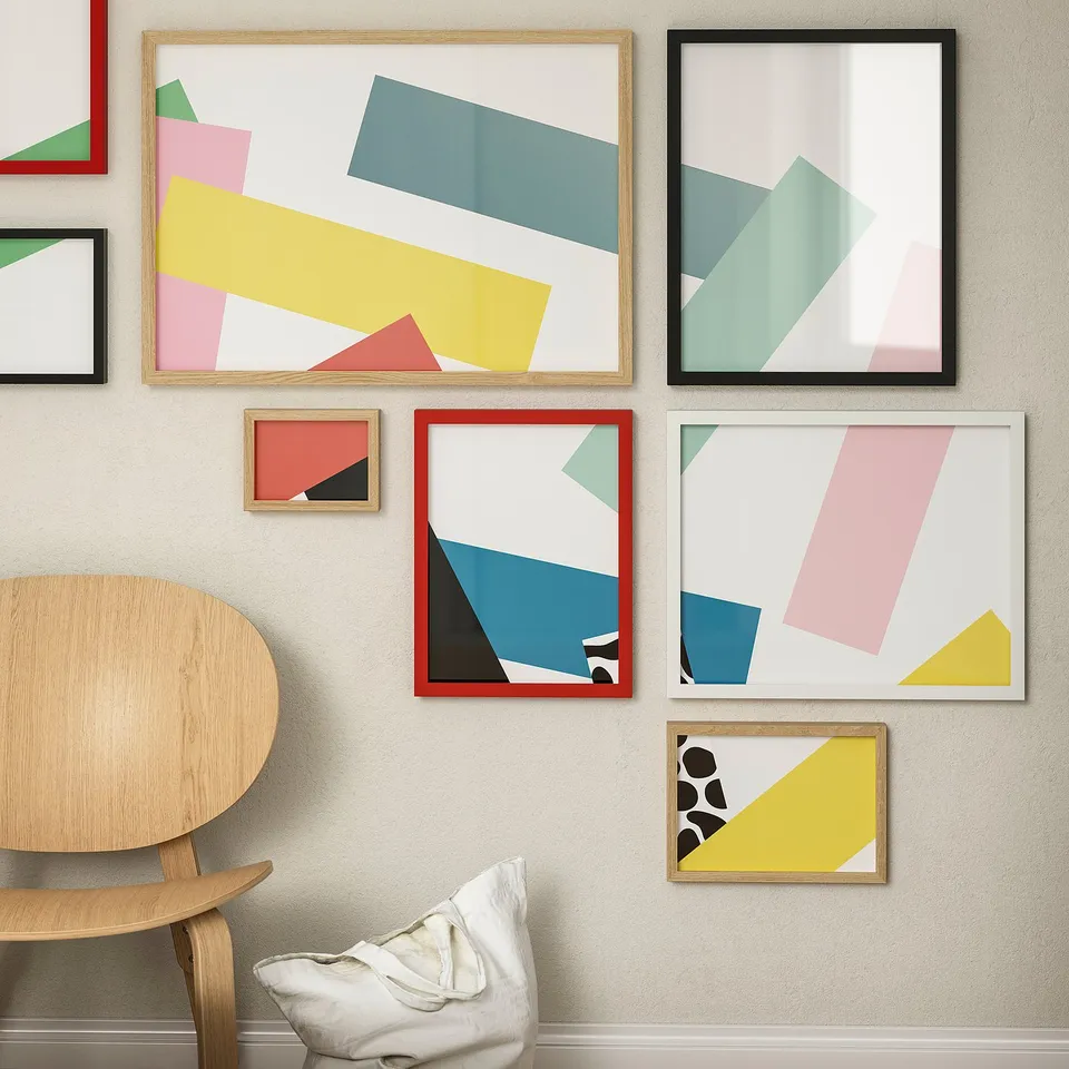 Six colourful geometric art prints, including a large wooden frame, on a wall, contrasting with white chair and bean bag below.