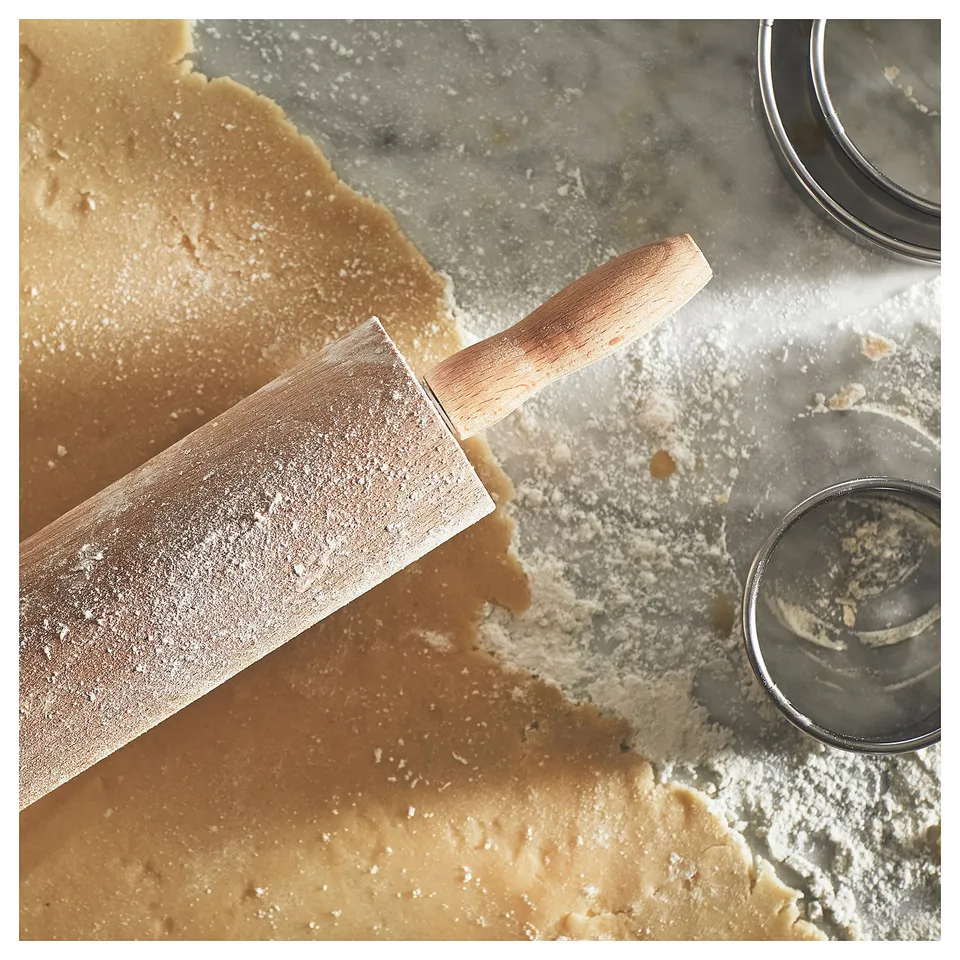 Wooden rolling pin on floured marble counter, next to metal cookie cutter.