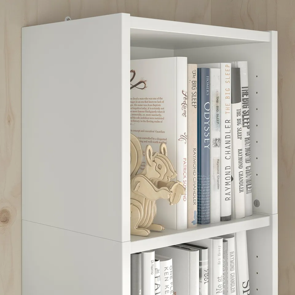 A white BILLY bookcase with adjustable shelves holding various books and a wooden decorative squirrel figure.