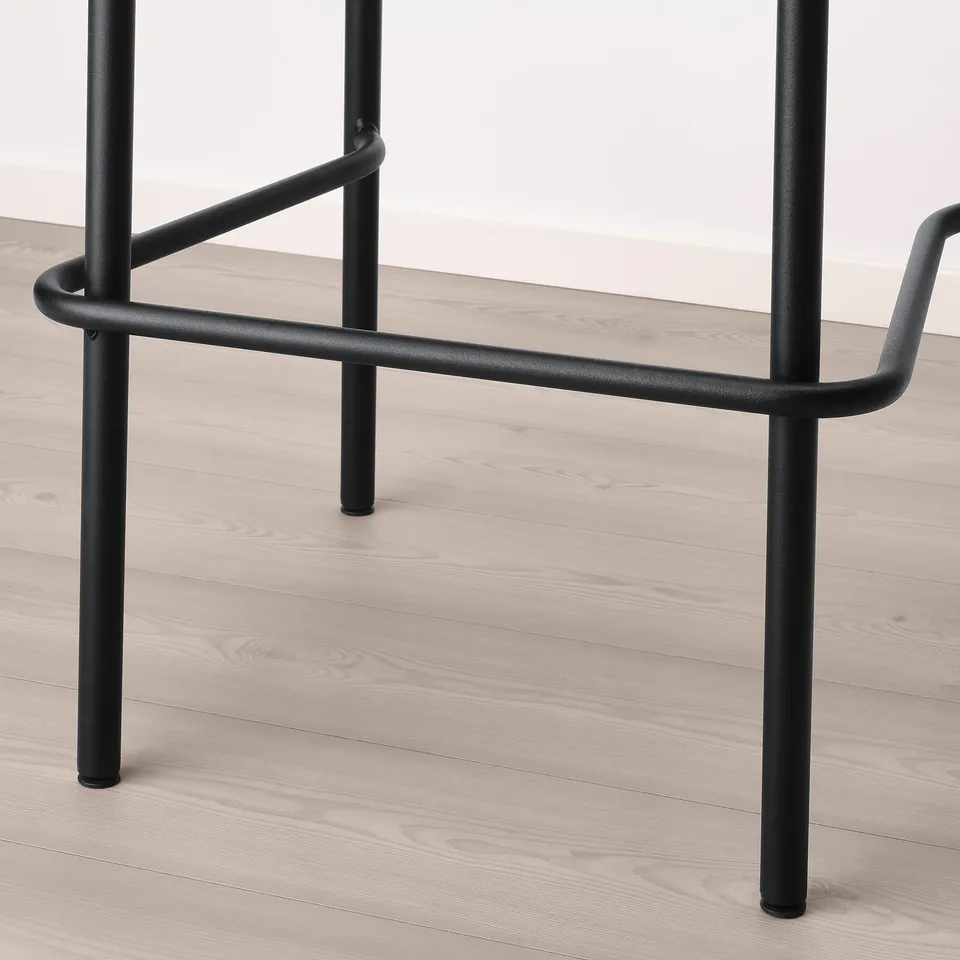 Black metal bar stool with curved back support, sturdy legs, on wooden floor.